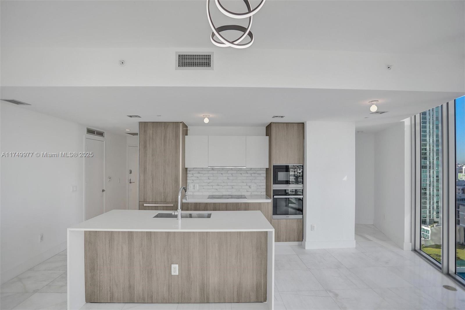 A modern kitchen features a white island, wood-toned cabinetry, and floor-to-ceiling windows — 2900 NE 7th Ave # 1601, Miami FL 33137, MIAMI, FL