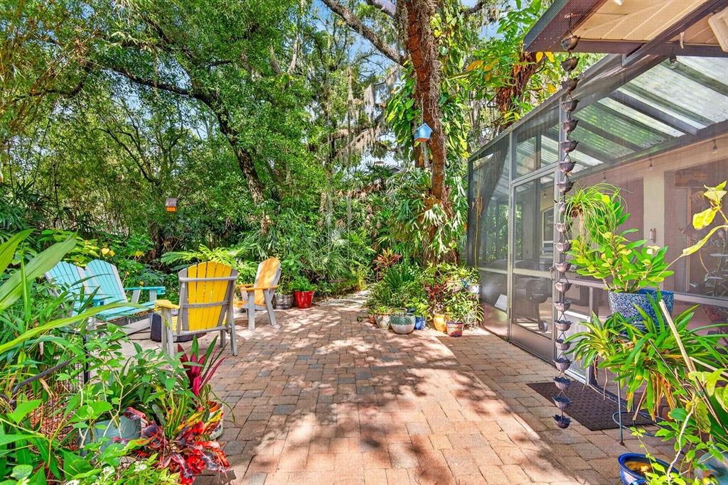 A brick patio features colorful Adirondack chairs and lush landscaping next to a screened-in porch — 2073 MISTY SUNRISE TRAIL, SARASOTA, FL
