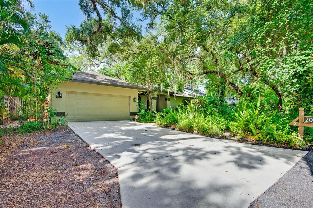 A single-story house with a beige garage and driveway surrounded by lush green trees — 2073 MISTY SUNRISE TRAIL, SARASOTA, FL