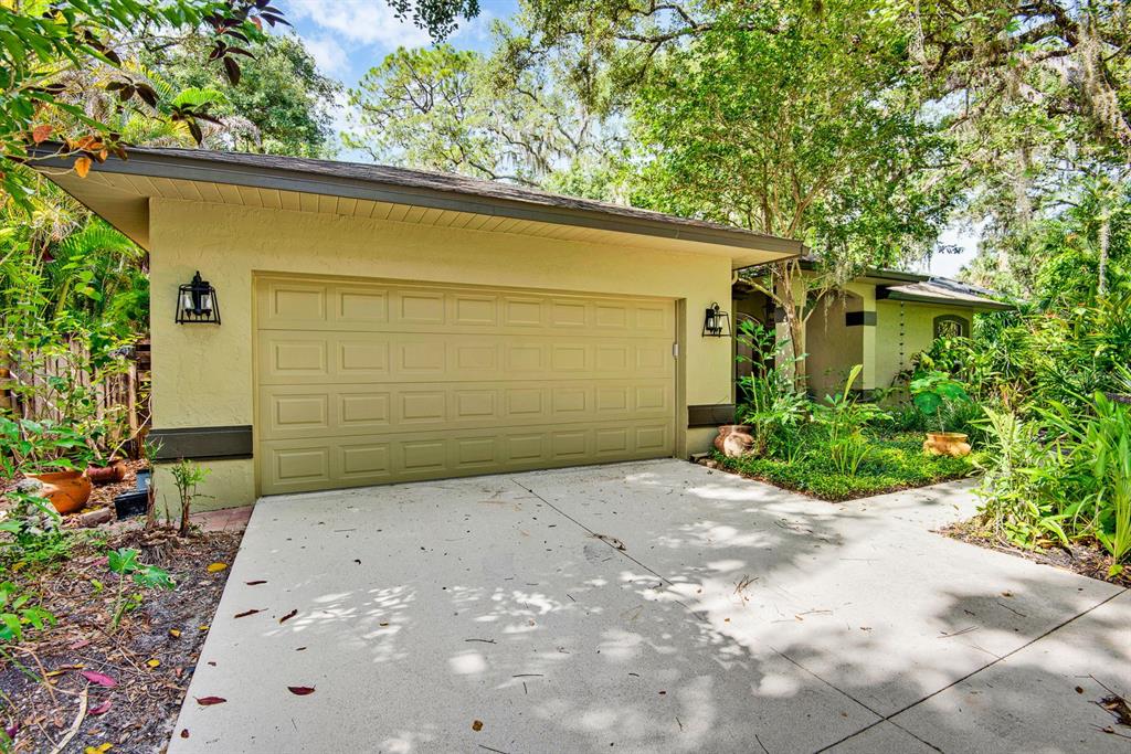 A beige house with a two-car garage and a concrete driveway surrounded by lush landscaping — 2073 MISTY SUNRISE TRAIL, SARASOTA, FL