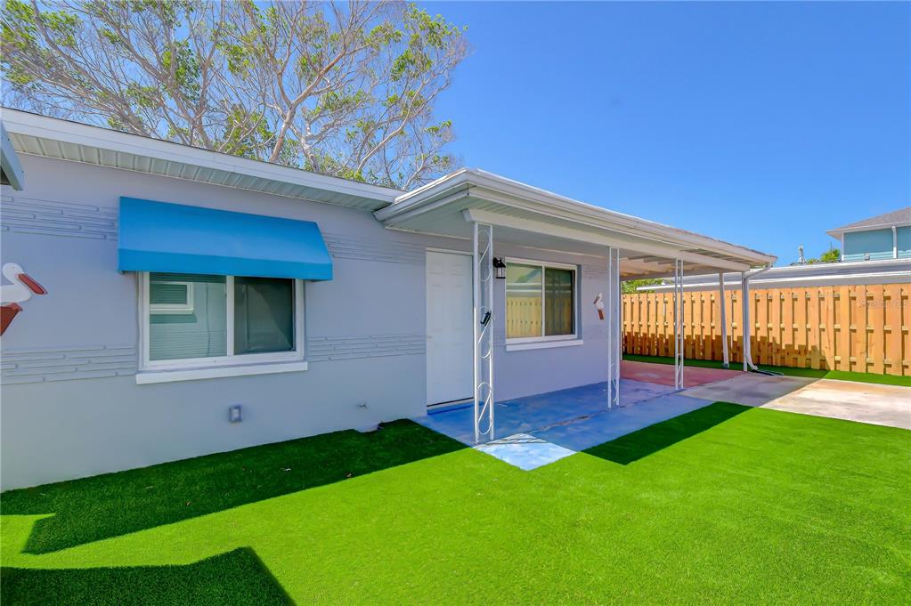 A light blue house exterior features a covered porch, artificial turf, and a wooden fence — 190 73RD AVENUE UNIT C, ST PETE BEACH, FL
