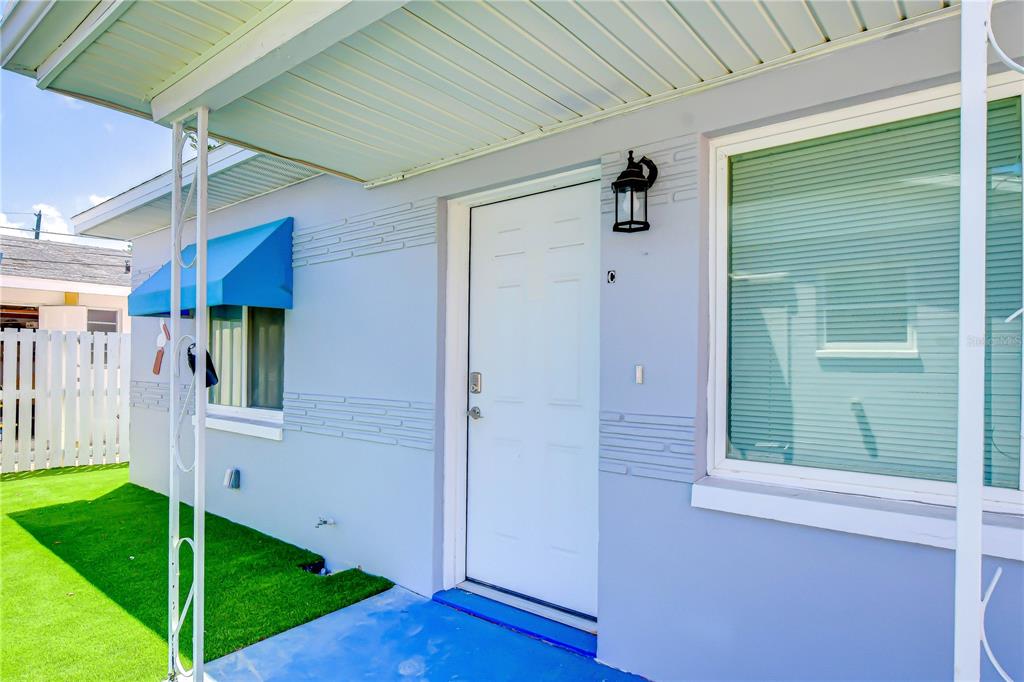 A light blue exterior wall features a white front door, a window, and an awning — 190 73RD AVENUE UNIT C, ST PETE BEACH, FL