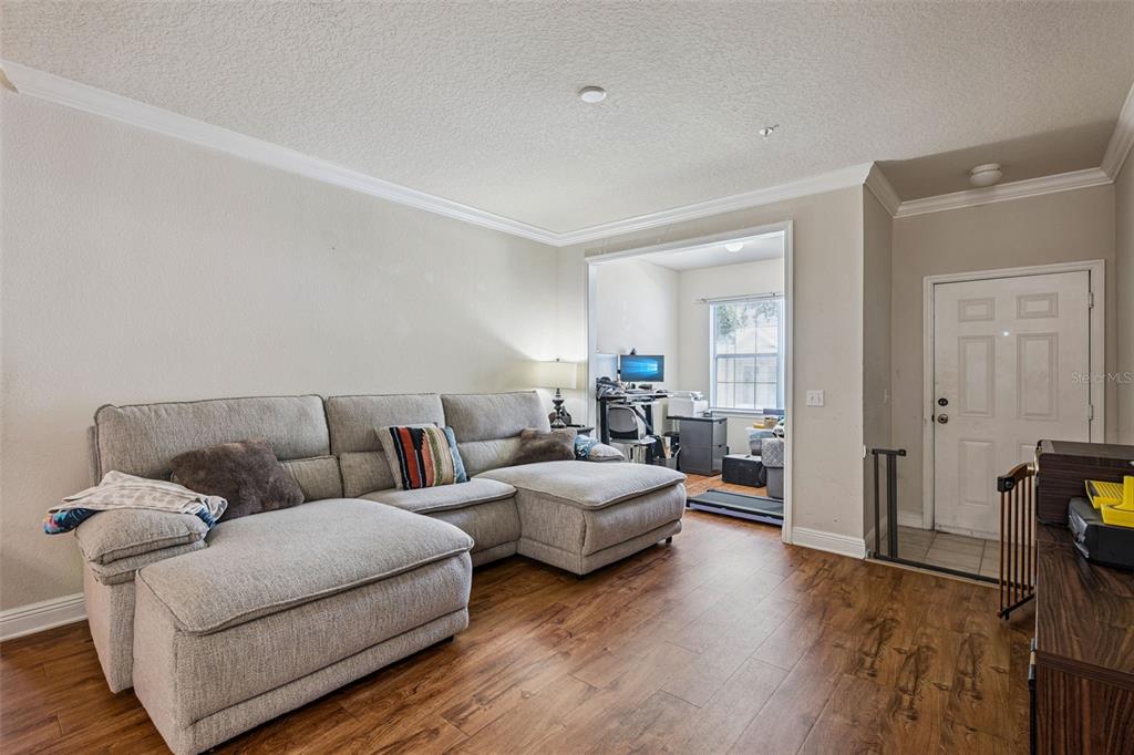 A living room features a large gray sectional sofa, wood-look flooring, and an adjacent office — 200 SOUTHERN PECAN CIRCLE UNIT 104, WINTER GARDEN, FL