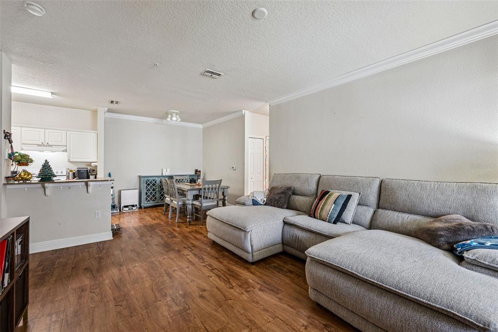 A living room with a gray sectional sofa, wood-look flooring, and an adjacent dining area — 200 SOUTHERN PECAN CIRCLE UNIT 104, WINTER GARDEN, FL