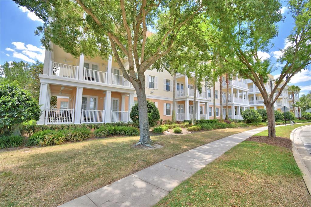 A multi-story apartment building with balconies and white railings sits behind a sidewalk and trees — 7480 EXCITEMENT DRIVE UNIT 102, REUNION, FL