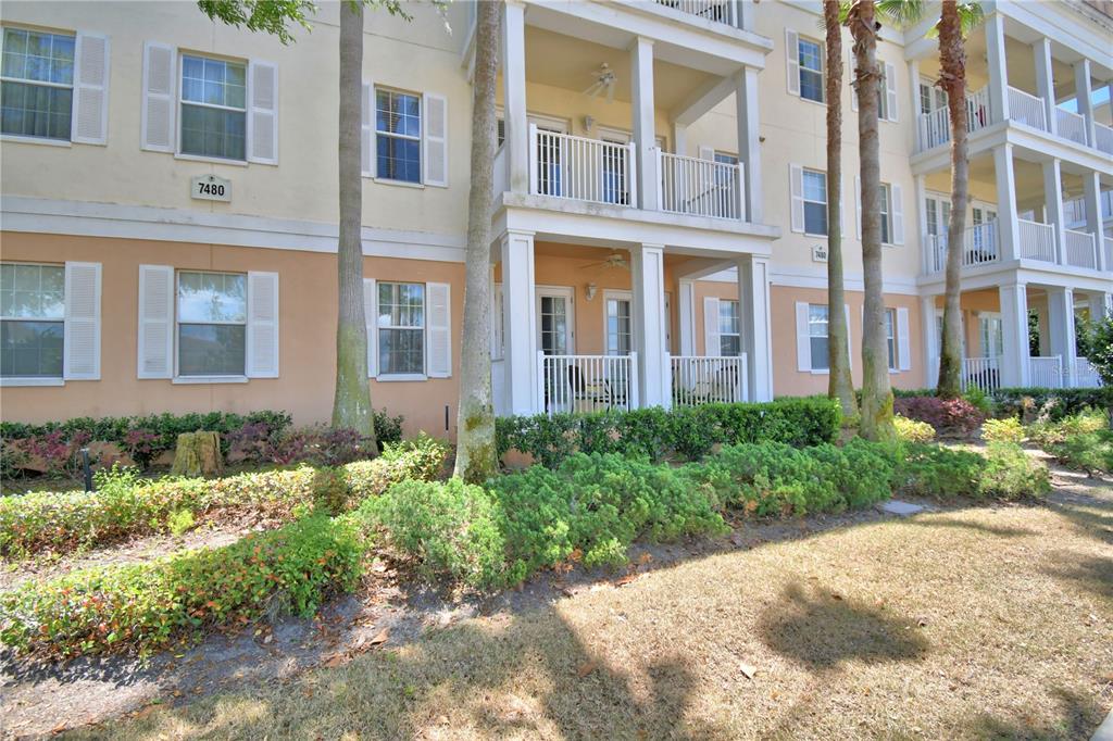 The exterior of a multi-story apartment building features balconies, white railings, and landscaped shrubbery — 7480 EXCITEMENT DRIVE UNIT 102, REUNION, FL