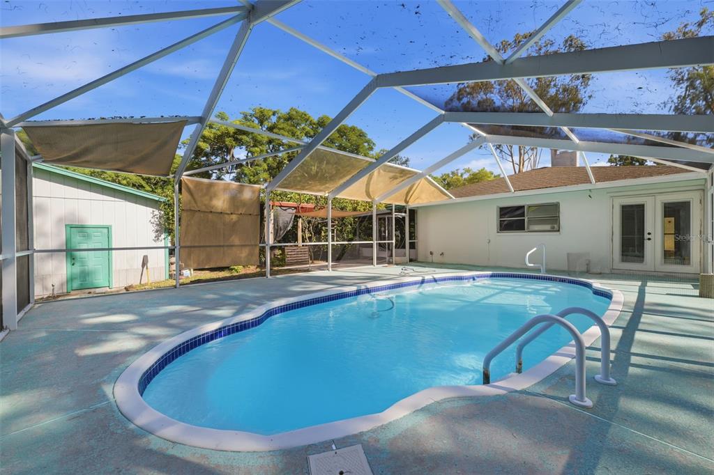A swimming pool with a metal ladder sits inside a screened-in patio area — 9116 LAKEVIEW DRIVE, NEW PORT RICHEY, FL