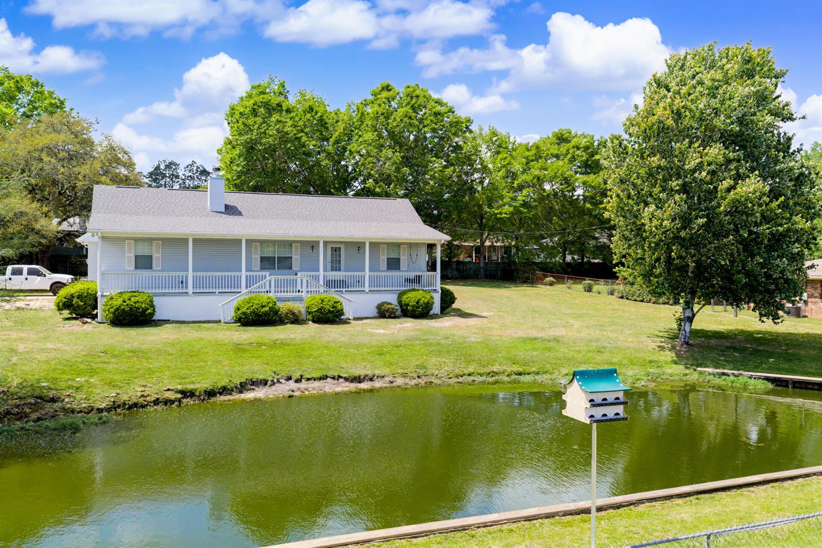 A light blue house with a front porch sits behind a pond and lawn — 7327 Glidden Lane, FL 32526, FL