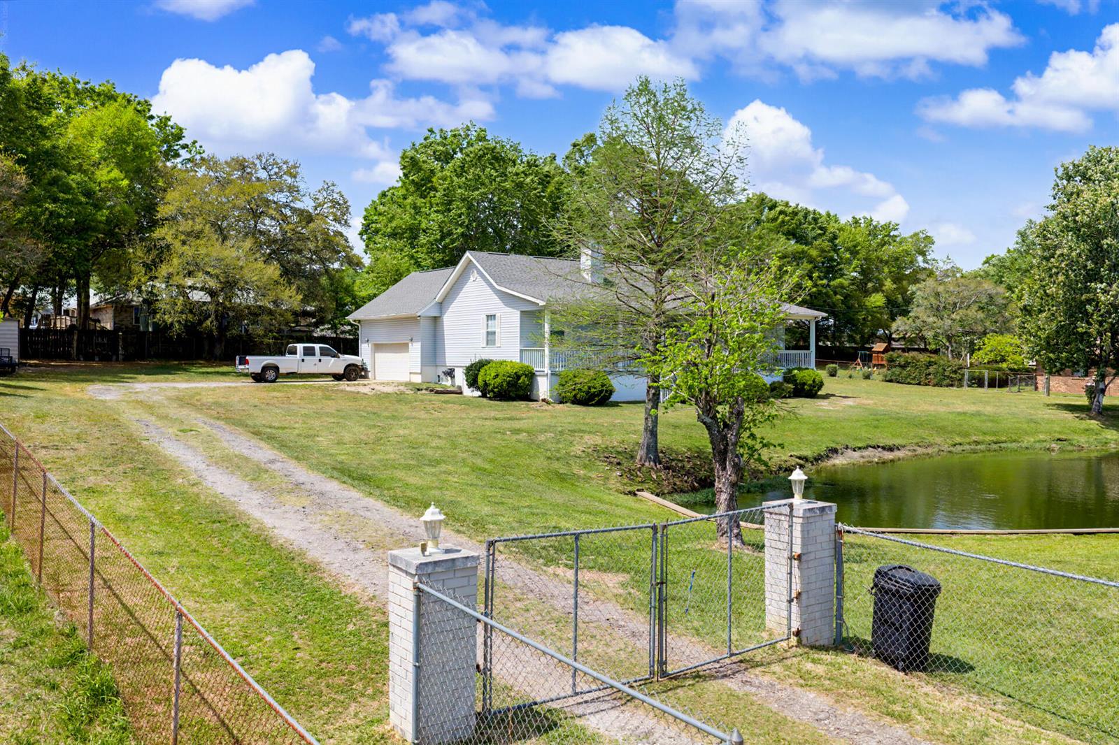 A white house with a gravel driveway and a pond sits behind a chain-link fence — 7327 Glidden Lane, FL 32526, FL