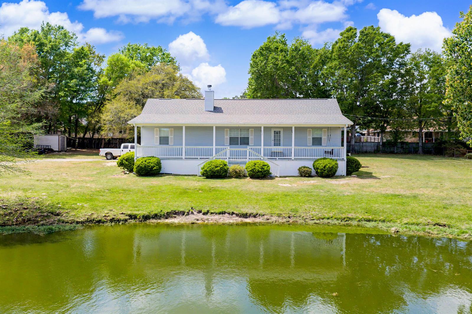 A light blue house with a front porch sits behind a pond under a blue sky — 7327 Glidden Lane, FL 32526, FL