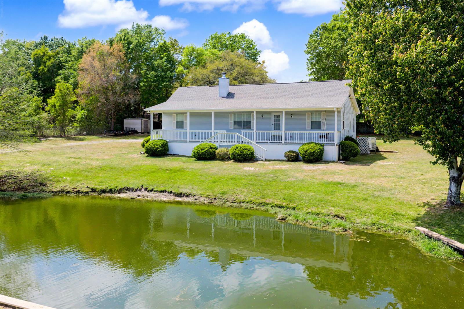 A light blue house with a front porch sits behind a pond on a lawn — 7327 Glidden Lane, FL 32526, FL