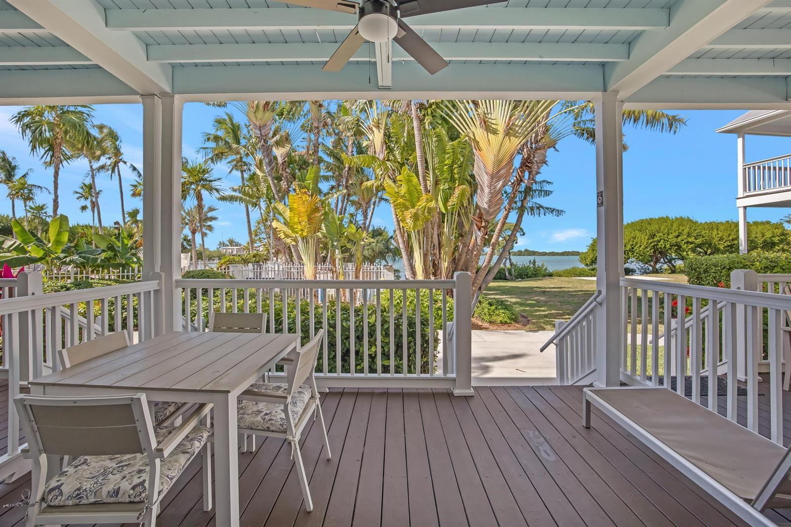 A covered wooden deck features a dining set and bench overlooking a tropical waterfront view — 5081 Sunset Village Drive, FL 33050, FL