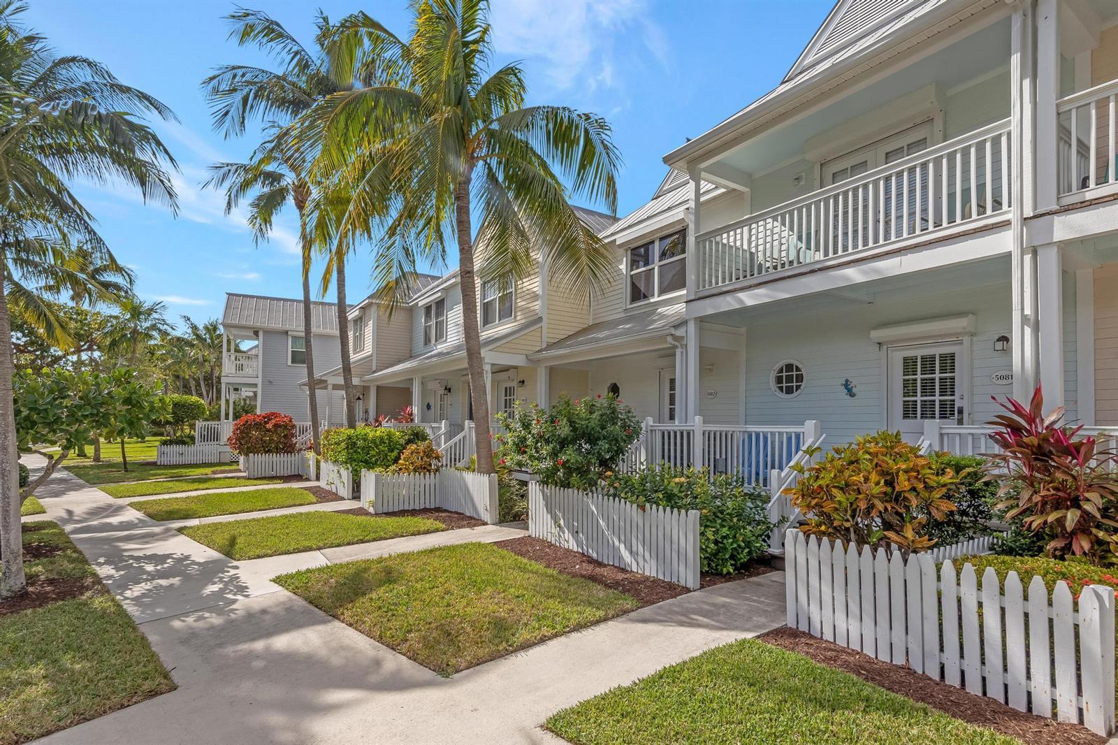 A row of light-colored townhouses with white picket fences and palm trees under a blue sky — 5081 Sunset Village Drive, FL 33050, FL