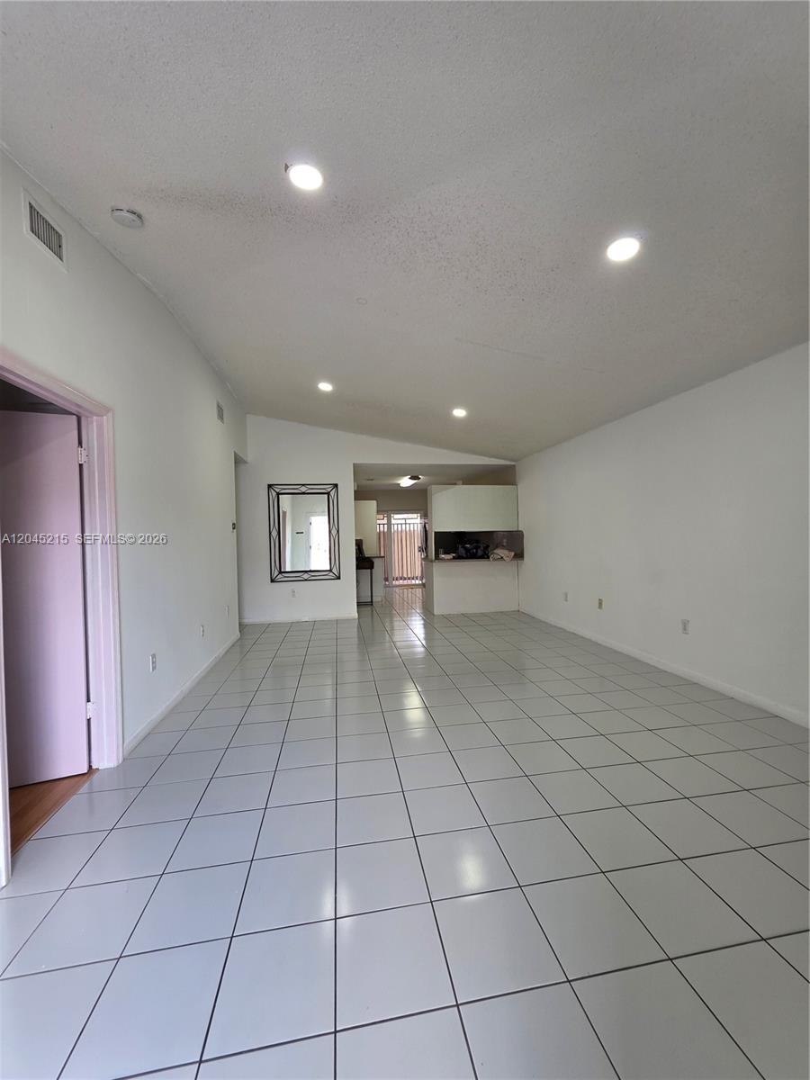An empty room features white walls, light-colored floor tiles, recessed lighting, and a vaulted ceiling — 8905 NW 121 ST # 0, Hialeah FL 33018, HIALEAH, FL