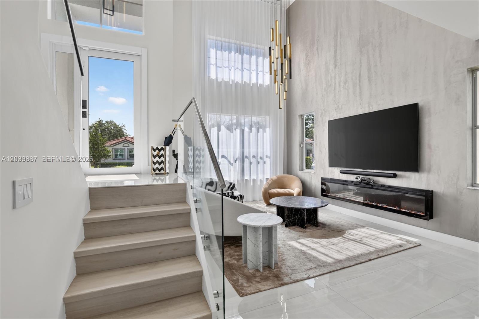 A modern living room features a floating fireplace, a large television, and a glass staircase — 16233 Opal Creek Dr, Weston FL 33331, WESTON, FL