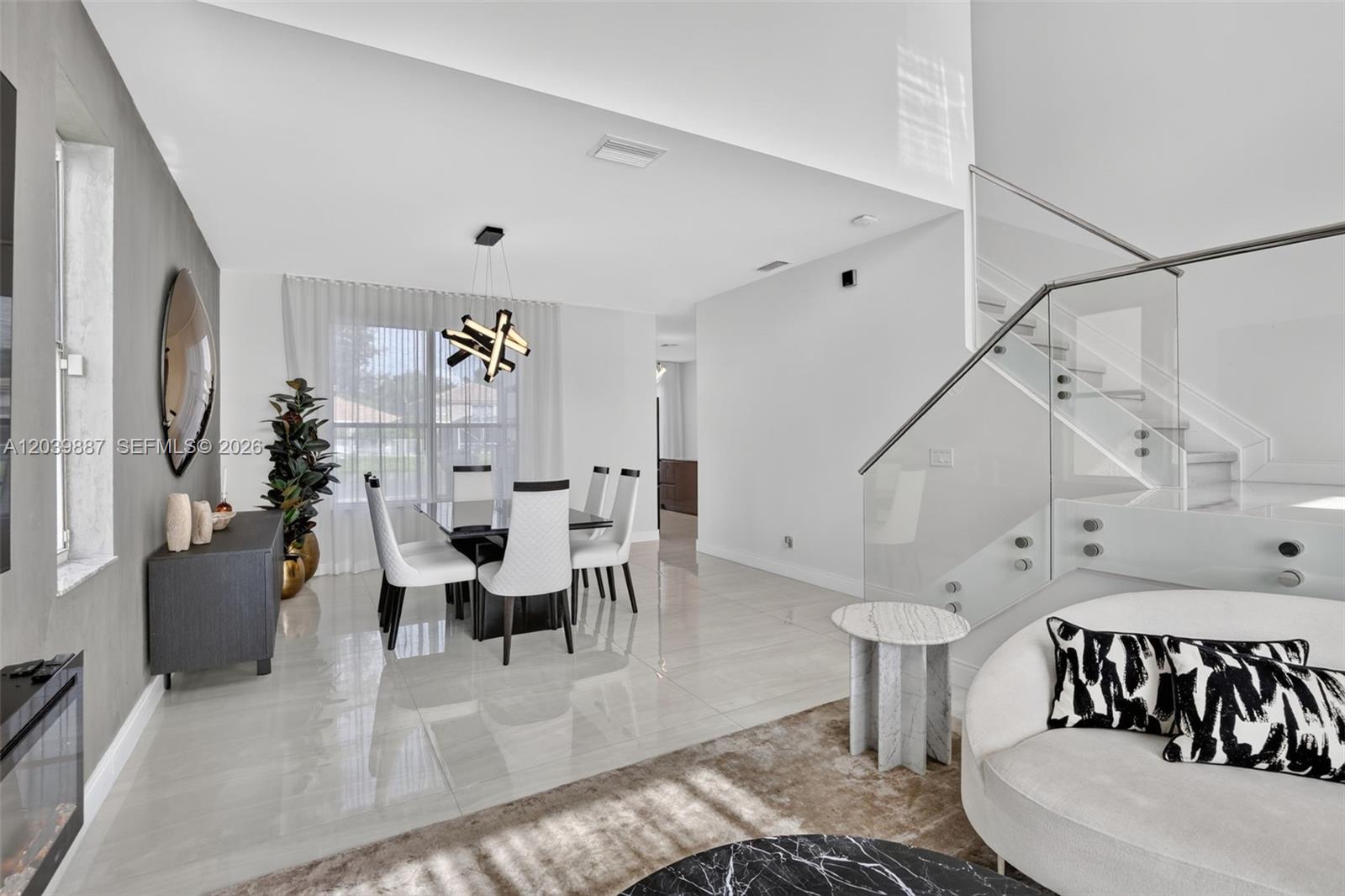 A modern dining area features a glass table, sculptural chandelier, and a glass-railed staircase — 16233 Opal Creek Dr, Weston FL 33331, WESTON, FL