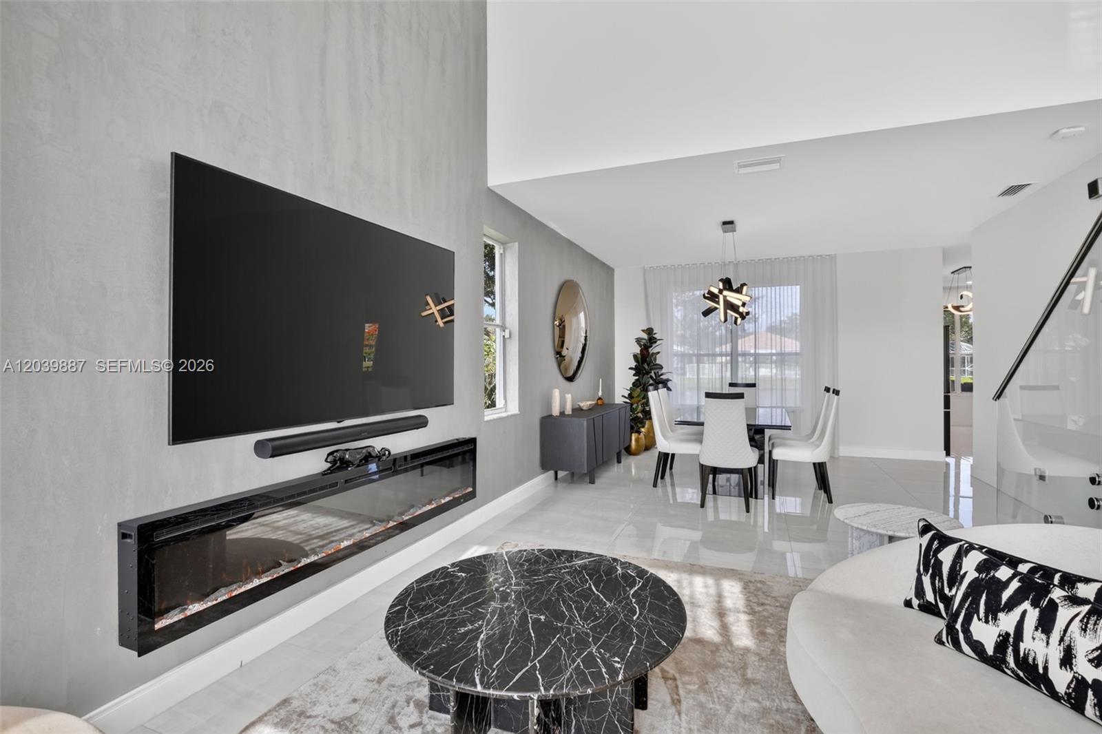 A modern living and dining room features a wall-mounted television, fireplace, and marble coffee table — 16233 Opal Creek Dr, Weston FL 33331, WESTON, FL