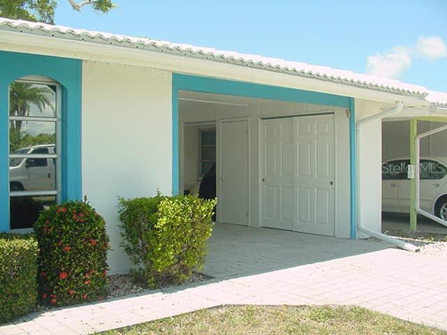 A white house exterior features a turquoise-trimmed window, a covered carport, and a paved driveway — 533 CIRCLEWOOD DRIVE, VENICE, FL