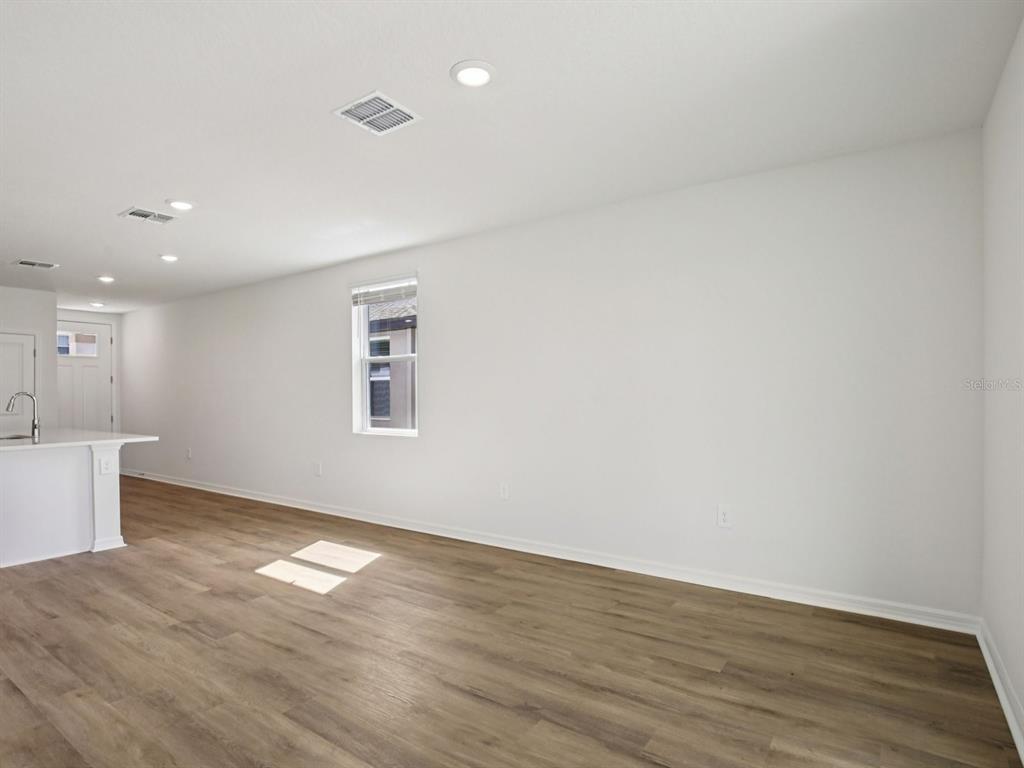 An empty room with white walls, wood-look flooring, recessed lighting, and a kitchen counter — 11321 BELLEWOOD TERRACE, PARRISH, FL