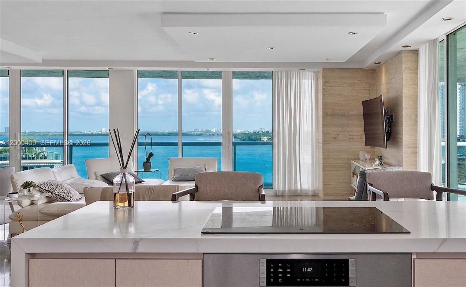 A modern kitchen island with a cooktop overlooks a living area with floor-to-ceiling water views — 10 Venetian Way # 804, Miami Beach FL 33139, MIAMI BEACH, FL