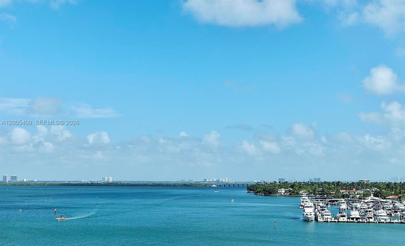 A view of a bay with a marina, boats, and a distant bridge under a blue sky — 10 Venetian Way # 804, Miami Beach FL 33139, MIAMI BEACH, FL