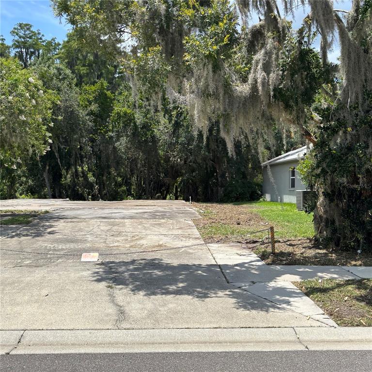 A concrete slab sits on a vacant residential lot next to a small house — 1323 BAYTHORN DRIVE, WESLEY CHAPEL, FL