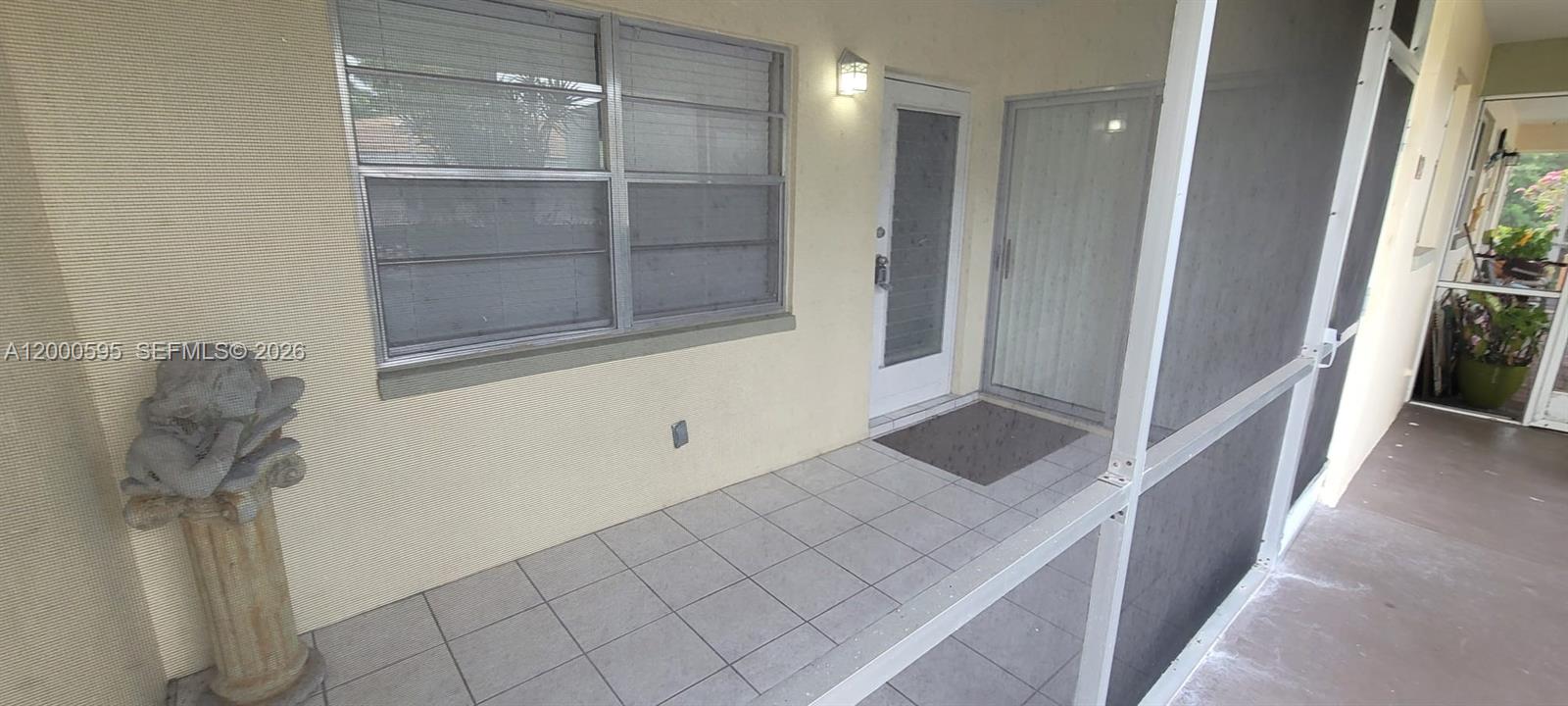 A screened-in patio features tiled flooring, a white door, and a decorative pedestal statue — 1340 NE 28th Ave # 129, Pompano Beach FL 33062, POMPANO BEACH, FL