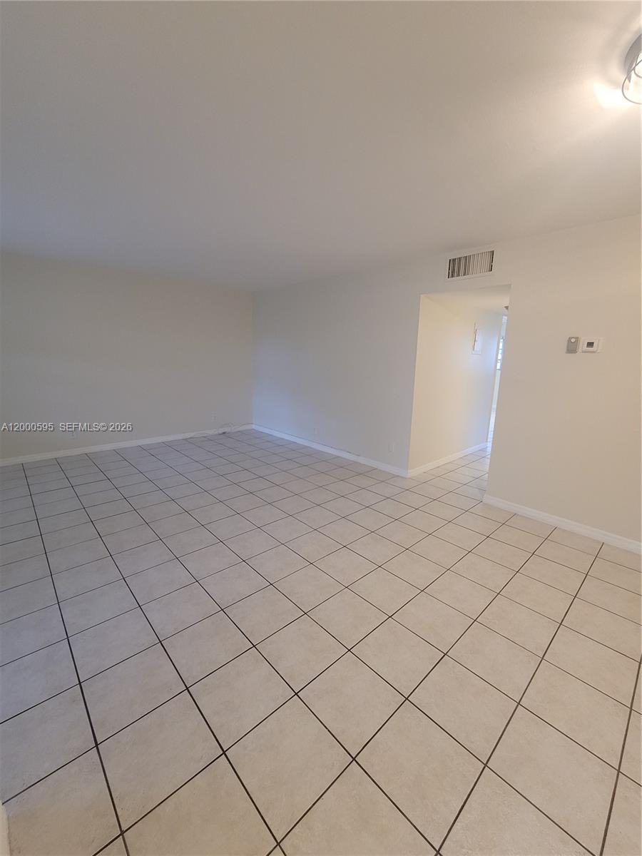 An empty room features white walls and light-colored square floor tiles — 1340 NE 28th Ave # 129, Pompano Beach FL 33062, POMPANO BEACH, FL