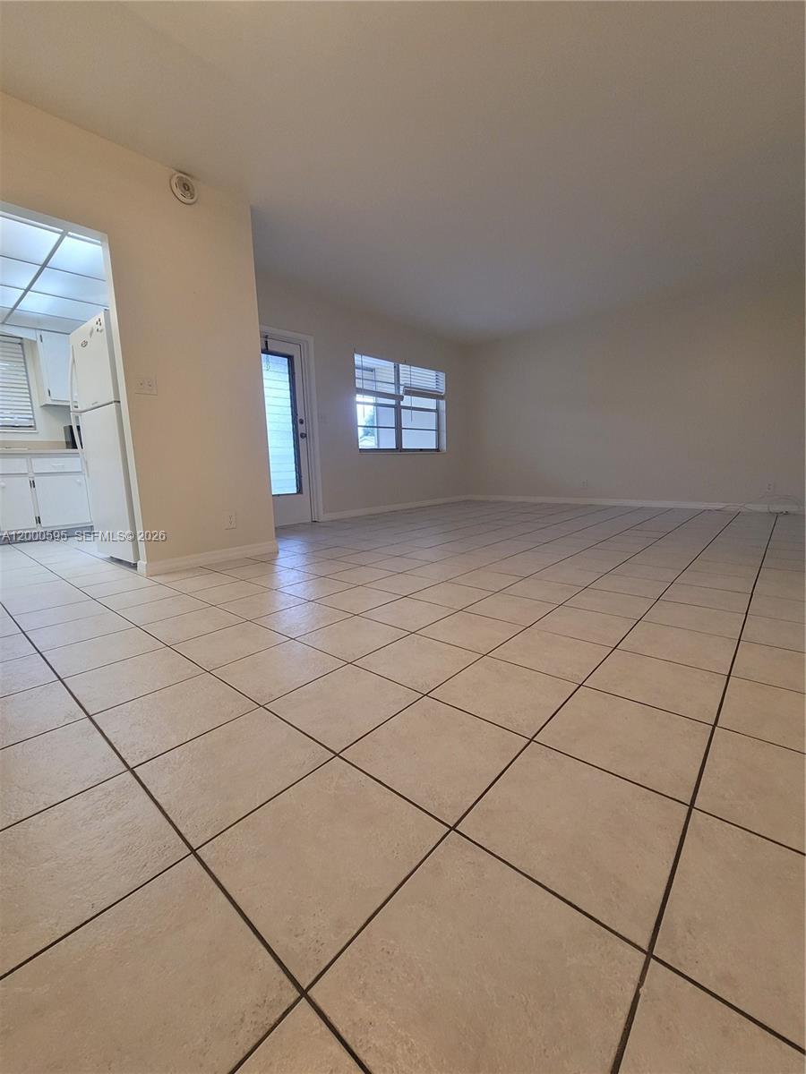 An empty room features light-colored tile flooring, beige walls, a window, and a glass-paneled door — 1340 NE 28th Ave # 129, Pompano Beach FL 33062, POMPANO BEACH, FL