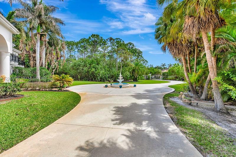 A circular driveway with a central fountain leads toward a house surrounded by palm trees — 2584 SE Ranch Acres Cir, Jupiter FL 33478, JUPITER, FL