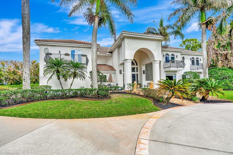 A two-story white stucco house features a large arched entryway, balconies, and palm trees — 2584 SE Ranch Acres Cir, Jupiter FL 33478, JUPITER, FL