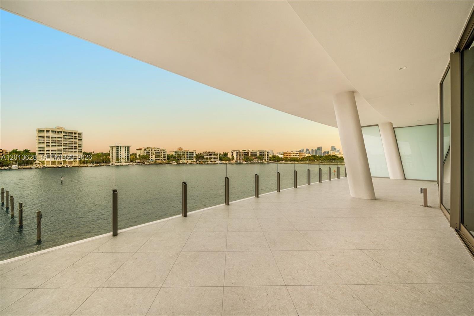 A spacious balcony with light-colored tile flooring overlooks a body of water and city skyline — 5 Grove Isle Dr # S302, Coconut Grove FL 33133, COCONUT GROVE, FL
