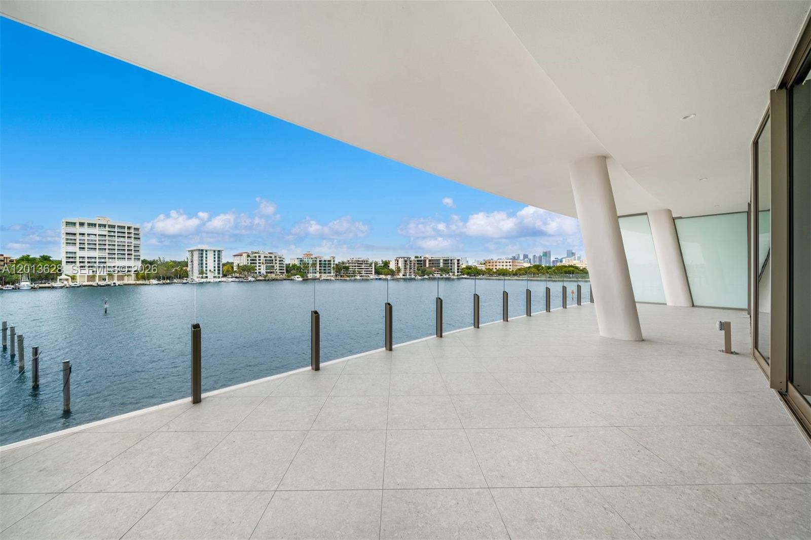 A spacious, tiled balcony overlooks a body of water with a city skyline in the distance — 5 Grove Isle Dr # S302, Coconut Grove FL 33133, COCONUT GROVE, FL