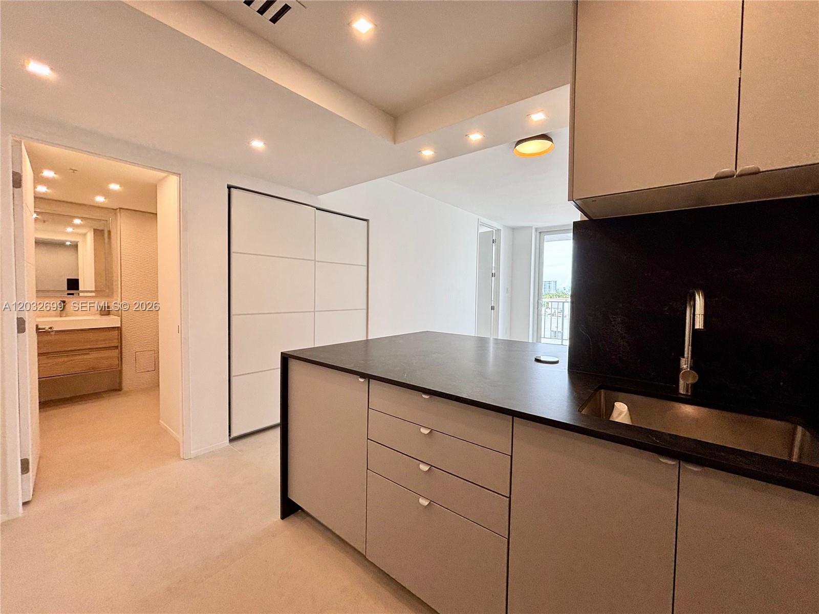 A modern kitchen features dark countertops, light cabinetry, and an adjacent bathroom with wood vanity — 2829 Indian Creek Dr # 604, Miami Beach FL 33140, MIAMI BEACH, FL