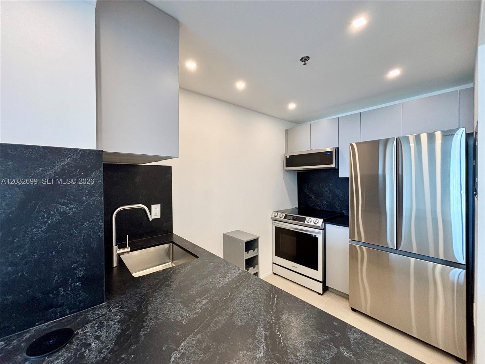 A modern kitchen features dark stone countertops, stainless steel appliances, and light gray cabinetry — 2829 Indian Creek Dr # 604, Miami Beach FL 33140, MIAMI BEACH, FL