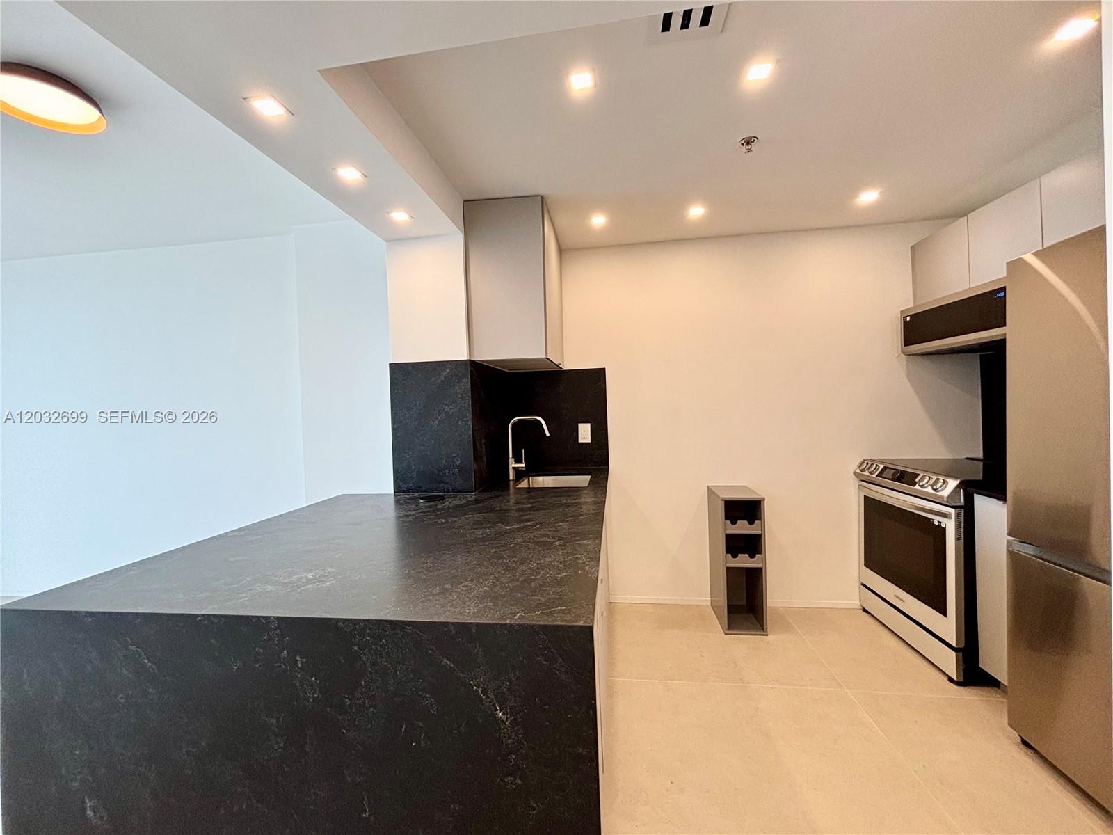 A modern kitchen features dark stone countertops, stainless steel appliances, and recessed ceiling lighting — 2829 Indian Creek Dr # 604, Miami Beach FL 33140, MIAMI BEACH, FL