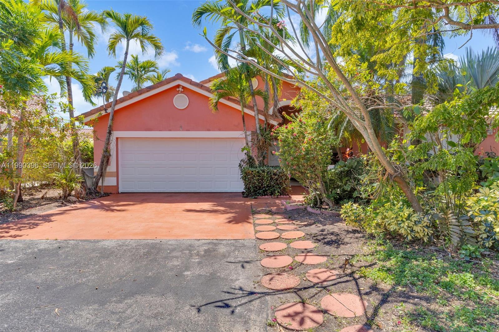 A peach-colored house features a white garage door, a driveway, and a stone walkway — 15012 SW 45th Ln, Miami FL 33185, MIAMI, FL