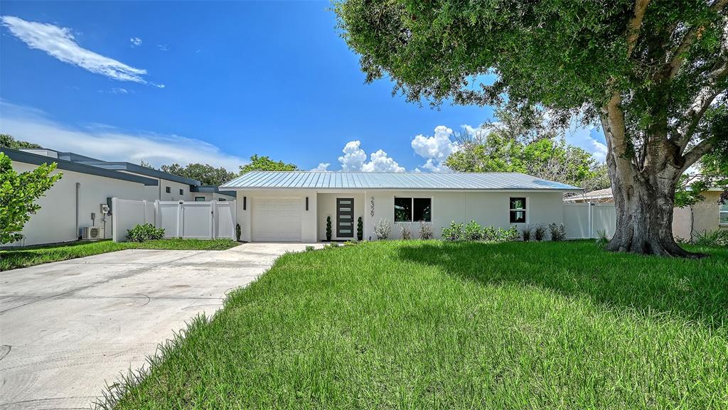 A single-story house with a white exterior, metal roof, and a large tree in front — 2329 ROSE STREET, SARASOTA, FL
