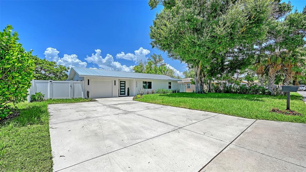 A single-story house with a white exterior, metal roof, and concrete driveway under a blue sky — 2329 ROSE STREET, SARASOTA, FL