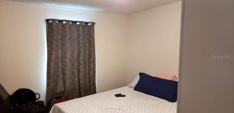 A bedroom features a bed with a blue pillow and a window with dark curtains — 1089 GREENSKEEP DRIVE, KISSIMMEE, FL