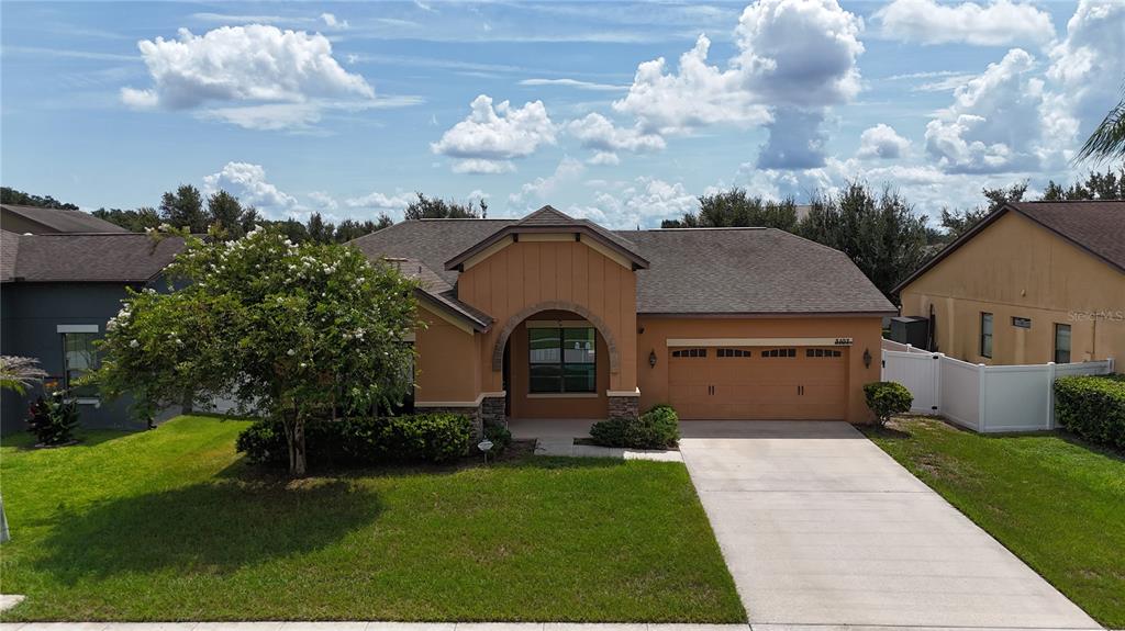 A single-story suburban house with a tan stucco exterior, a two-car garage, and a lawn — 3107 HARRIS PARK WAY, KISSIMMEE, FL