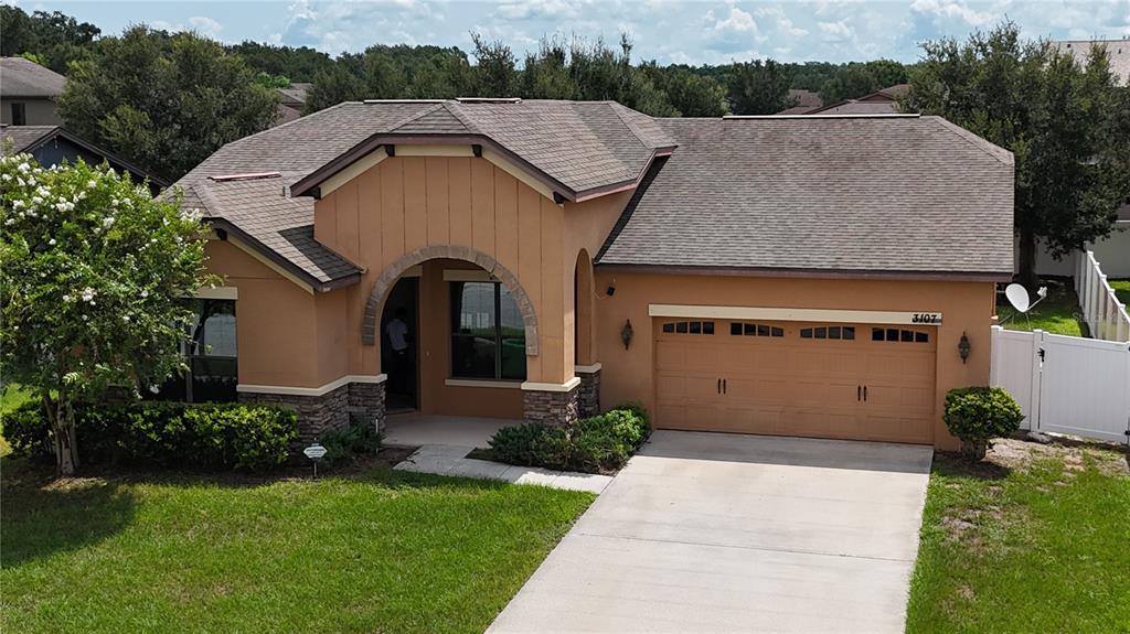 A single-story house with a tan stucco exterior, stone accents, and a two-car garage — 3107 HARRIS PARK WAY, KISSIMMEE, FL