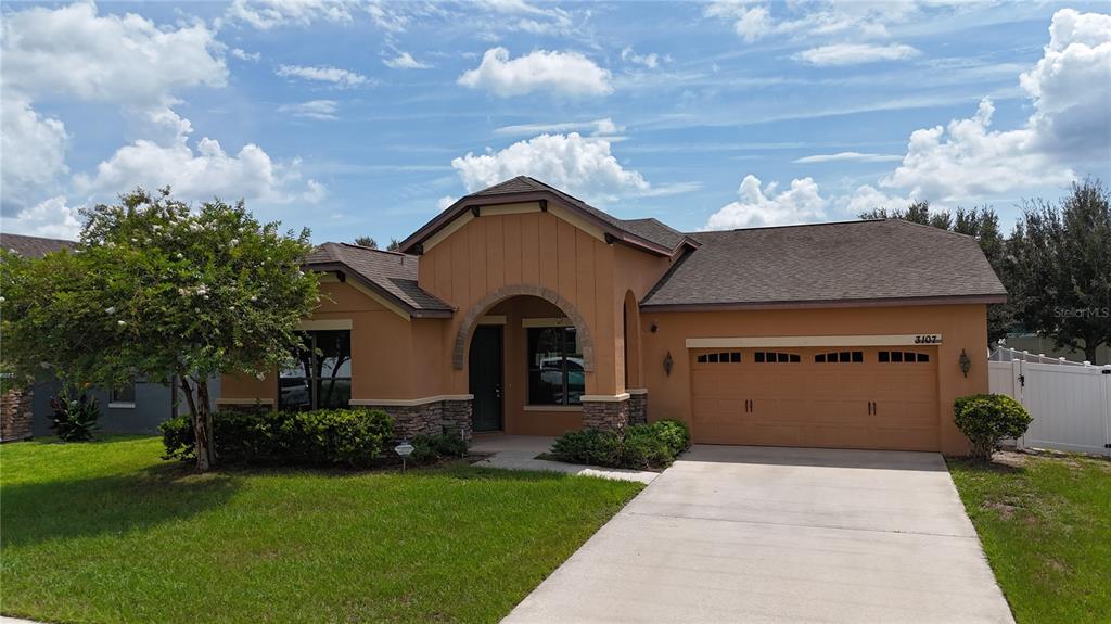 A single-story house with a tan stucco exterior, stone accents, and an attached two-car garage — 3107 HARRIS PARK WAY, KISSIMMEE, FL