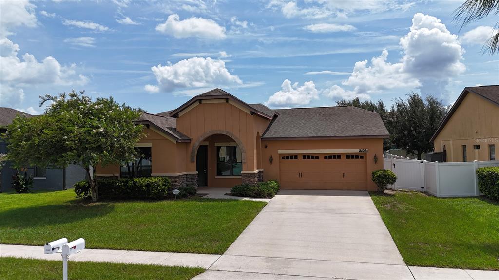 A single-story house with a tan stucco exterior, a two-car garage, and a front lawn — 3107 HARRIS PARK WAY, KISSIMMEE, FL