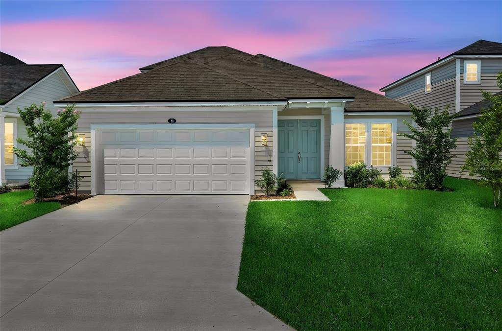 A single-story house with a two-car garage, light siding, and double front doors at dusk — 48 WINDMILL PALM WAY, PALM COAST, FL