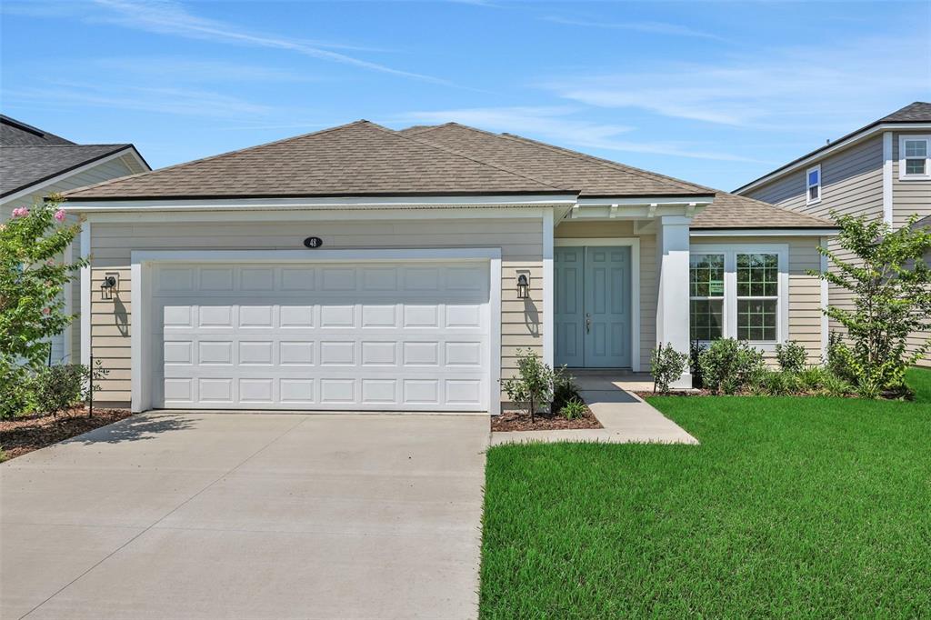 A single-story house with beige siding, a two-car garage, and a light blue front door — 48 WINDMILL PALM WAY, PALM COAST, FL