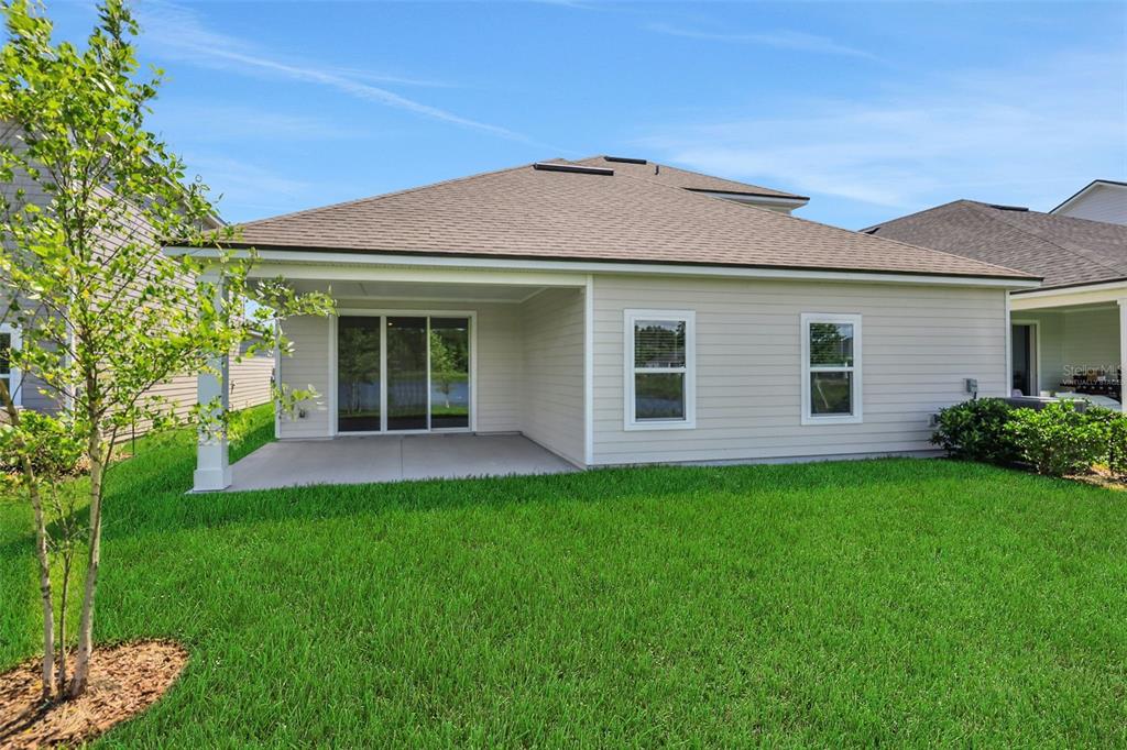 The exterior rear view of a house features a covered patio and a grassy yard — 48 WINDMILL PALM WAY, PALM COAST, FL