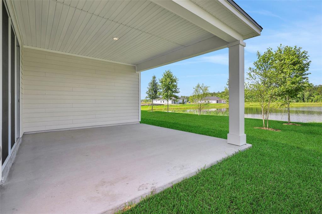 A covered concrete patio overlooks a grassy lawn and a pond under a blue sky — 48 WINDMILL PALM WAY, PALM COAST, FL