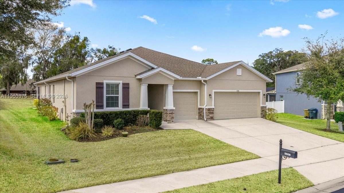 A single-story suburban house with a tan exterior, two-car garage, and a front lawn — 5608 SW 50th Ct, Ocala FL 34474, OCALA, FL