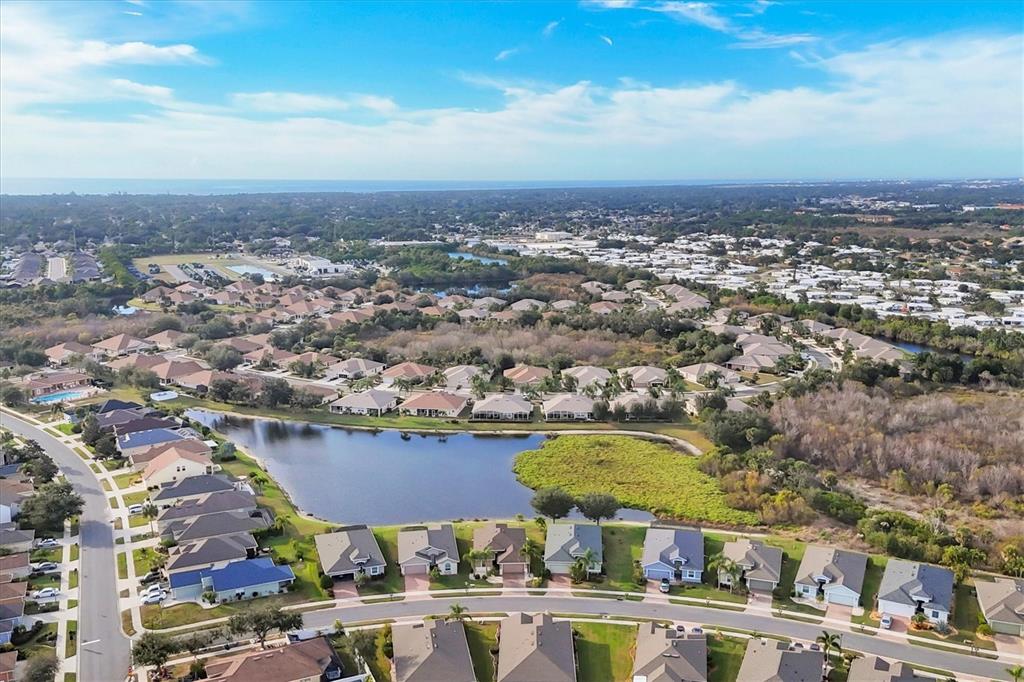 An aerial view shows a suburban neighborhood with houses surrounding a central pond — 5283 CANYONLAND WAY, VENICE, FL